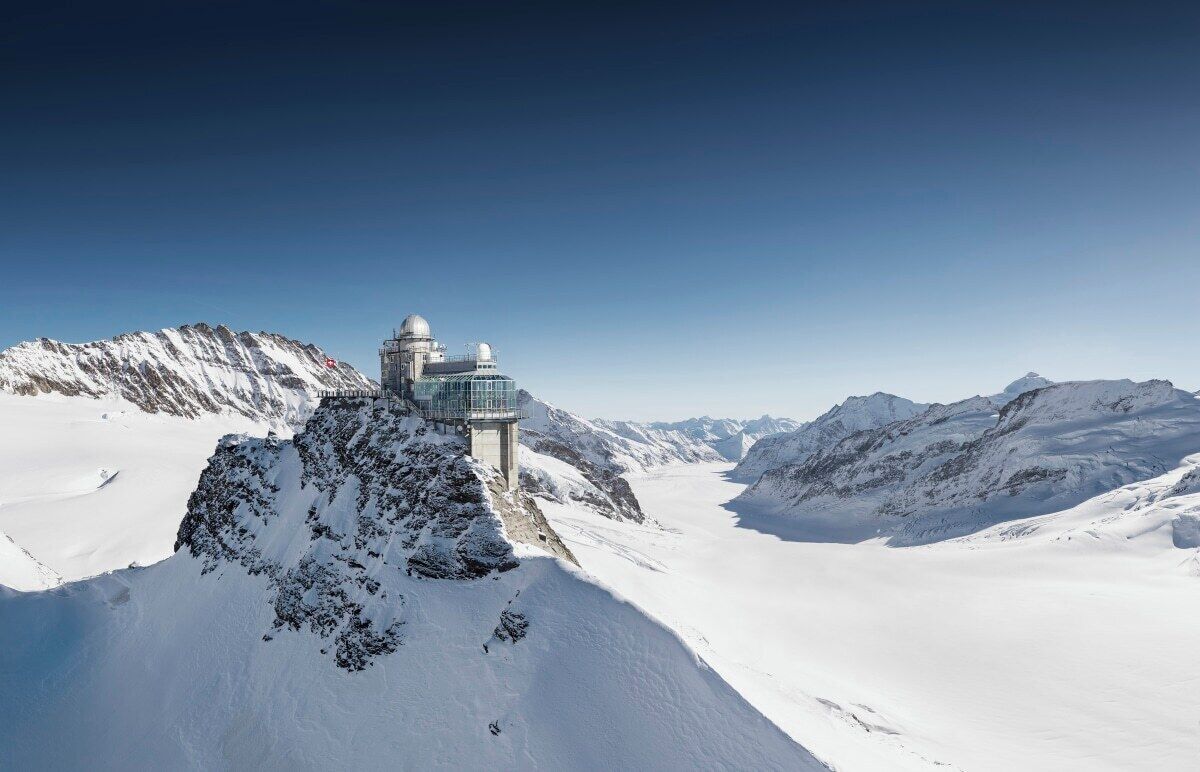 A snow-covered mountain with a modern observatory on a rocky outcrop.