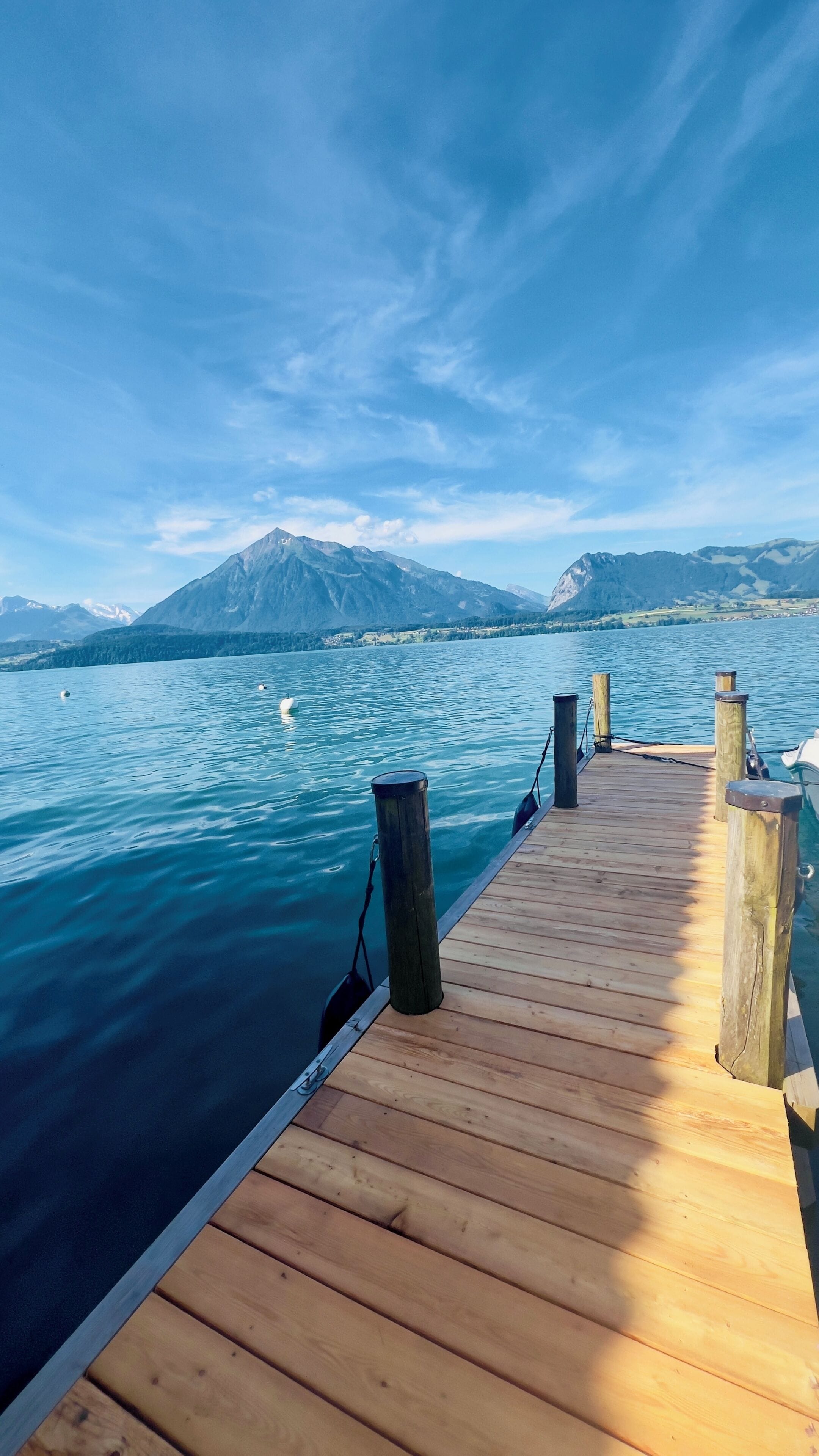 Un muelle de madera se adentra en un lago tranquilo, con una montaña al fondo.