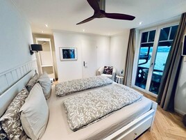 Un dormitorio con dos camas, un ventilador de techo, una ventana con vistas y una pequeña mesa con lámpara.