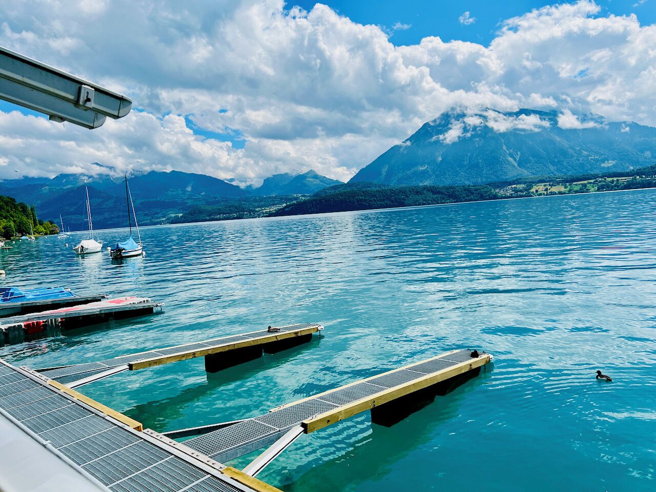 A calm lake with docked boats and a clear view of mountains in the background.
