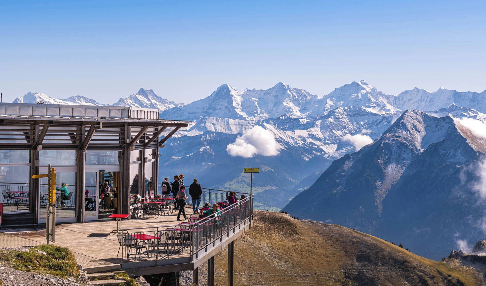A mountain observation deck with a glass enclosure, outdoor seating, and a view of snow-capped peaks.