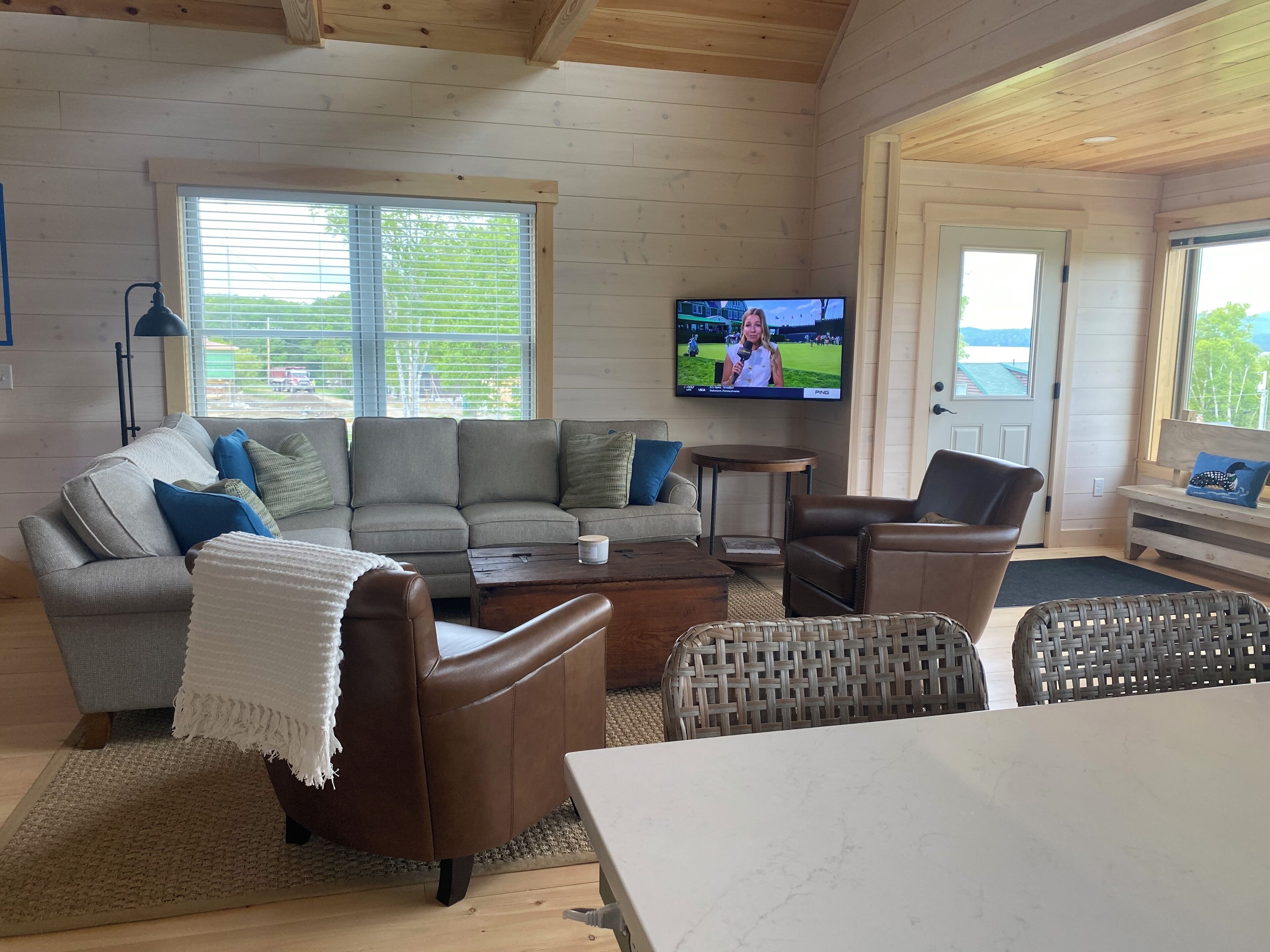 A cozy living room with a sectional sofa, leather armchairs, a coffee table, and a TV displaying a sports event.