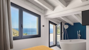 Een moderne badkamer met een vrijstaand bad, een groot raam met uitzicht op zee, en een schuifglazen deur naar een buitenruimte.