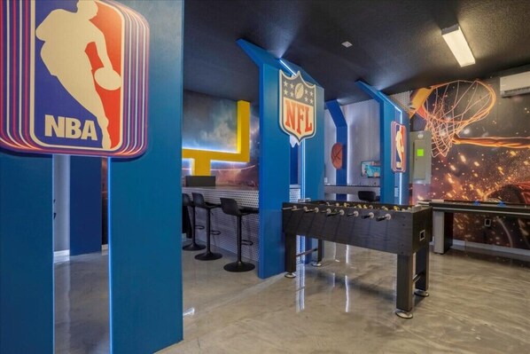 Une pièce décorée sur le thème du sport, avec des panneaux aux couleurs de la NBA et de la NFL, une table de baby-foot et un panier de basket.