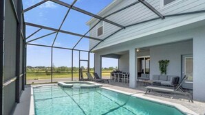 Une piscine à l’eau claire, entourée d’un patio couvert aménagé avec du mobilier d’extérieur et offrant une vue sur le paysage.