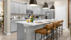 A modern kitchen with white cabinets, a central island with bar stools, and pendant lighting. - Last Minute Disney Getaway! Private Pool & Game Room. Book Now! #121741 (Orlando)