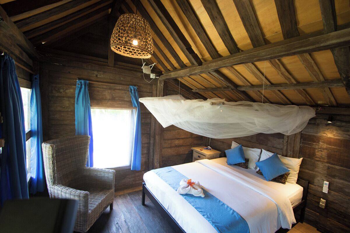 A wooden cabin bedroom with a bed, a chair, and a hanging mosquito net.