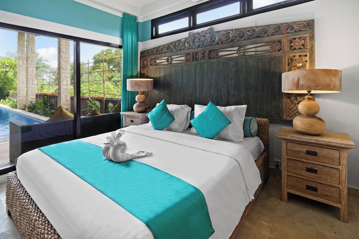 A large bed with a teal bedspread, two bedside tables with lamps, and a decorative headboard.