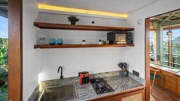 A kitchen with a granite countertop, stainless steel sink, and a built-in gas stove. There are wooden shelves above the countertop holding decorative items and a microwave.