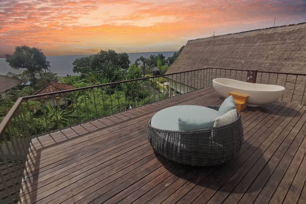 A wooden deck with a round wicker chair and a white bathtub.