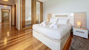 A modern bedroom with a large bed, wooden flooring, a wardrobe with mirrors, and bedside lamps. - Green Blue Horizon by Atlantic Holiday (São Vicente)