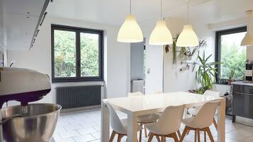 A modern kitchen with a white table, four chairs, pendant lights, and a large window.
