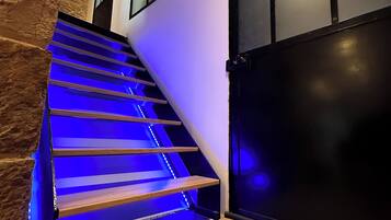 Een trap met blauwe LED-verlichting, een stenen muur en een zwarte deur.