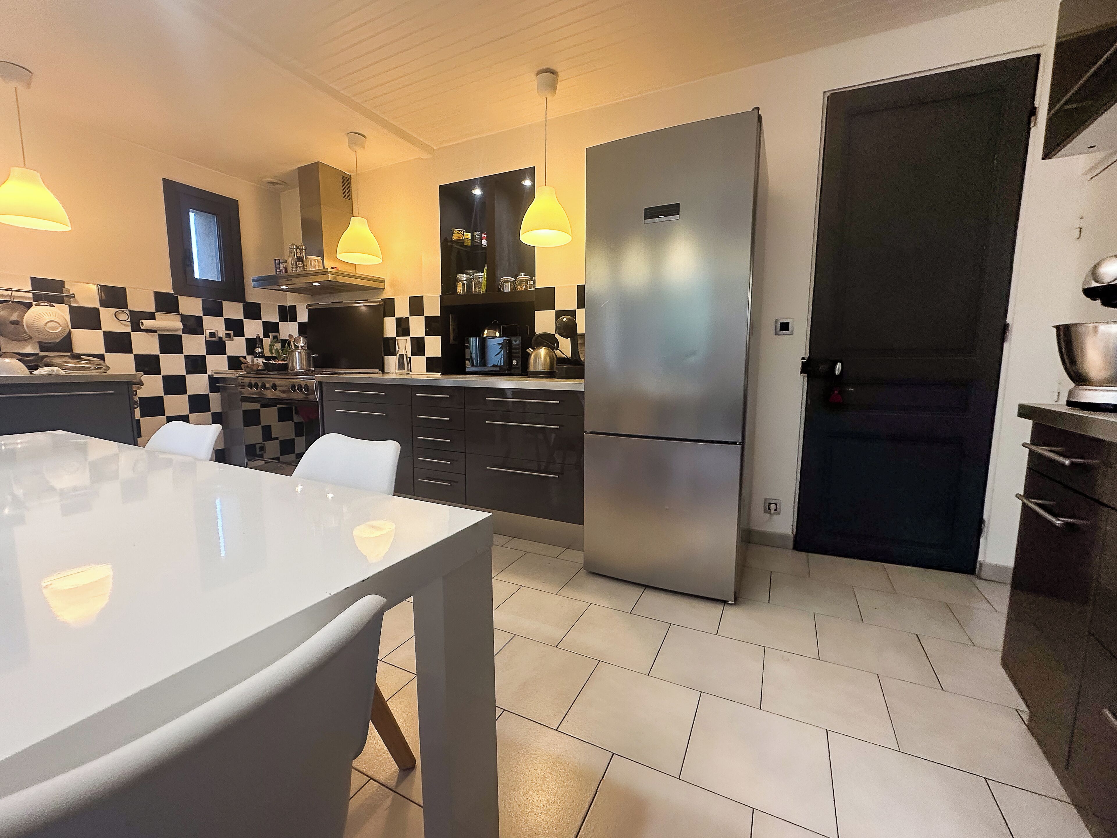 Een moderne keuken met een grote koelkast, een eettafel met stoelen en hanglampen.