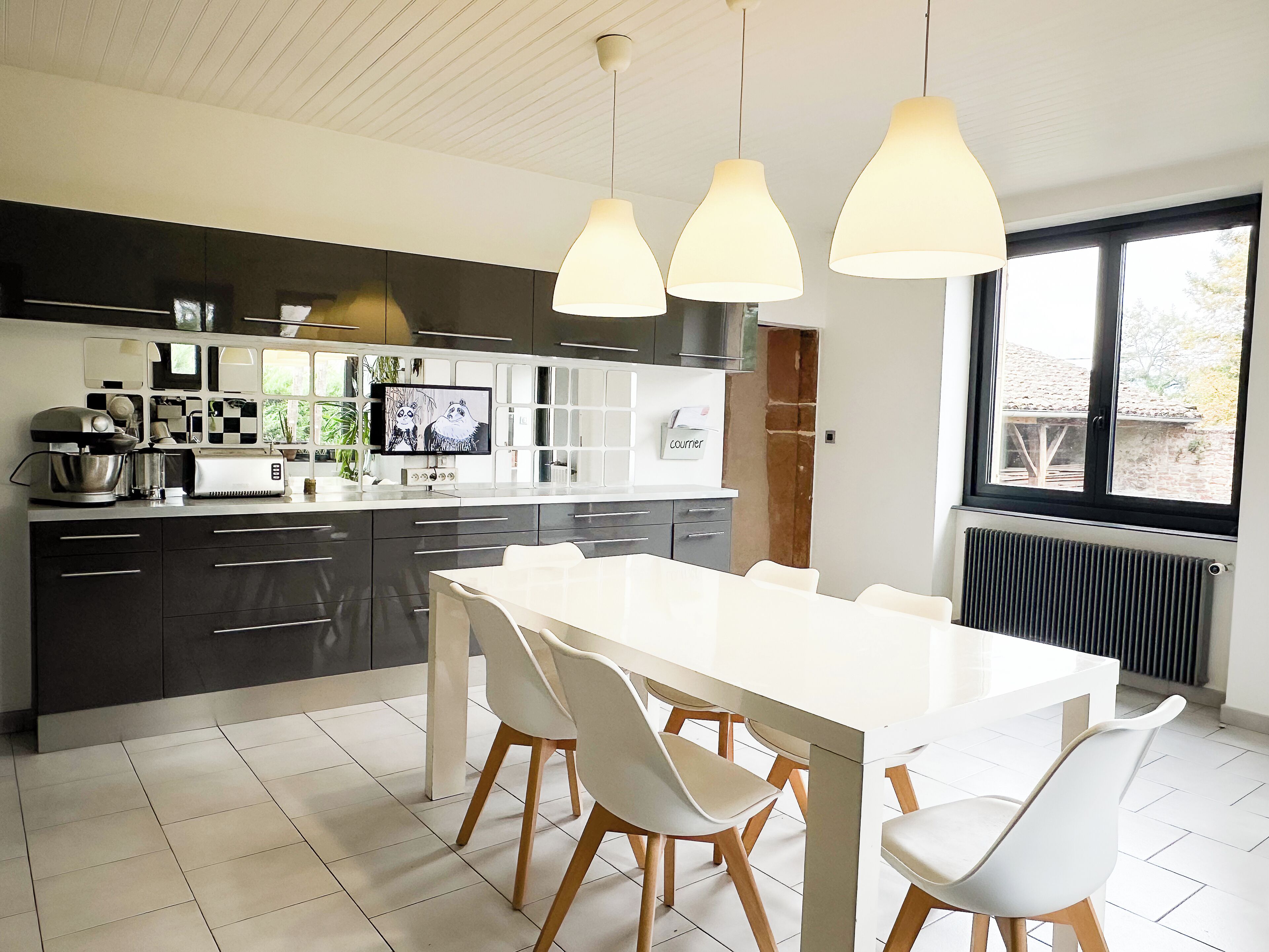 Una cucina moderna con un'isola grande, sedie bianche e lampade a sospensione.