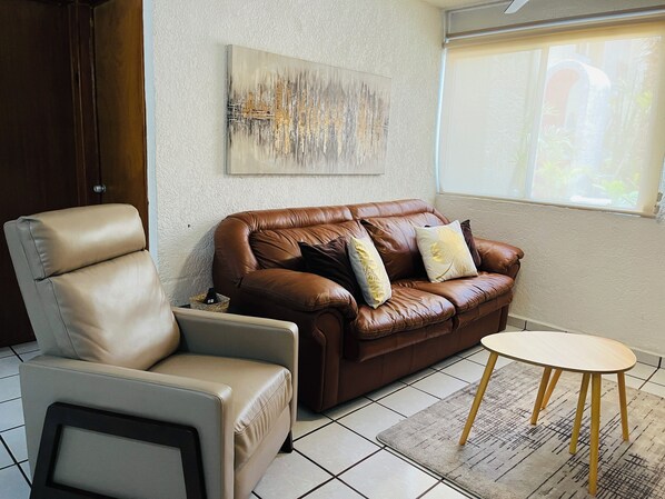 Ein Wohnzimmer mit einer braunen Ledersofa, einem beigen Sessel, einem kleinen runden Tisch und einem Gemälde an der Wand.