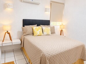 A hotel room with a bed, bedside lamps, a wall-mounted air conditioner, and a window.