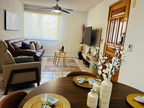 A living room with a sofa, TV, dining table, and a ceiling fan.