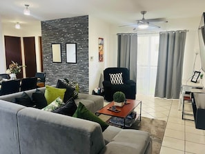 A modern living room with a grey sofa, a black armchair, a coffee table, and a dining area with a table and chairs.