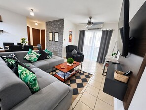 Una sala de estar moderna con un sofá, un sillón, una mesa de centro y un televisor de pantalla plana montado en la pared.