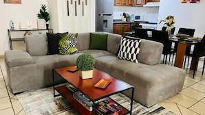 Ein Wohnzimmer mit grauem Ecksofa, einem Holztisch und einer kleinen Topfpflanze.