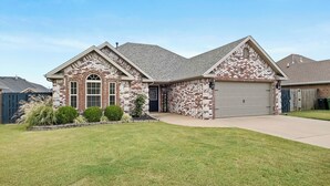 A two-story house with a brick facade, a garage, and a well-maintained lawn. - Greenway Getaway: Central to NWA & on the Razorback Greenway (Rogers)