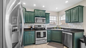 A modern kitchen with green cabinets, stainless steel appliances, and a black countertop. - Greenway Getaway: Central to NWA & on the Razorback Greenway (Rogers)