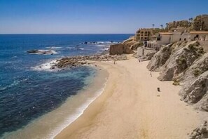 Une plage côtière avec un rivage rocheux, une eau d’un bleu limpide et des bâtiments situés sur le côté droit.