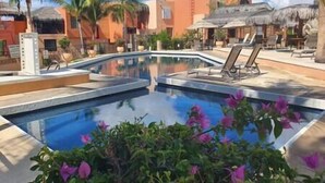 Ein Pool mit Liegestühlen, Palmen und einer Struktur mit Reetdach.
