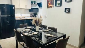 A modern kitchen with dark cabinetry, a black refrigerator, and a dining area with a glass table and chairs. - Chic Cabo Gateaway Walkable to Beach & Downtown Fun (Cabo San Lucas)