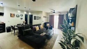 A modern living room with a black sofa, a dining table, and a ceiling fan. - Chic Cabo Gateaway Walkable to Beach & Downtown Fun (Cabo San Lucas)
