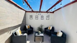 A covered patio area with two sofas and a small table, framed artwork on the wall, and a brick wall. - Chic Cabo Gateaway Walkable to Beach & Downtown Fun (Cabo San Lucas)