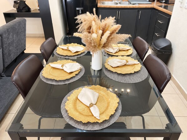 Una mesa de comedor preparada con individuales, servilletas y un florero con flores secas.