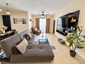 A modern living room with a sectional sofa, a flat-screen TV, and a potted plant. - Chic Cabo Gateaway Walkable to Beach & Downtown Fun (Cabo San Lucas)