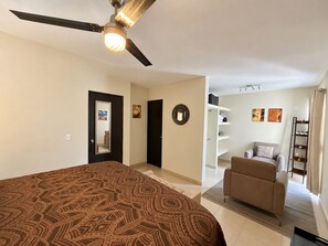 A bedroom with a bed, a ceiling fan, a wardrobe, a chair, and a shelf with decorative items. - Chic Cabo Gateaway Walkable to Beach & Downtown Fun (Cabo San Lucas)