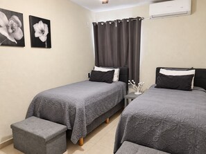 A hotel room with two beds, a small table, and a wall-mounted air conditioner.