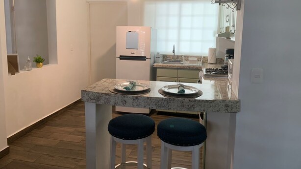Una cocina compacta con refrigerador, un lavamanos y una pequeña zona de comedor con dos taburetes.