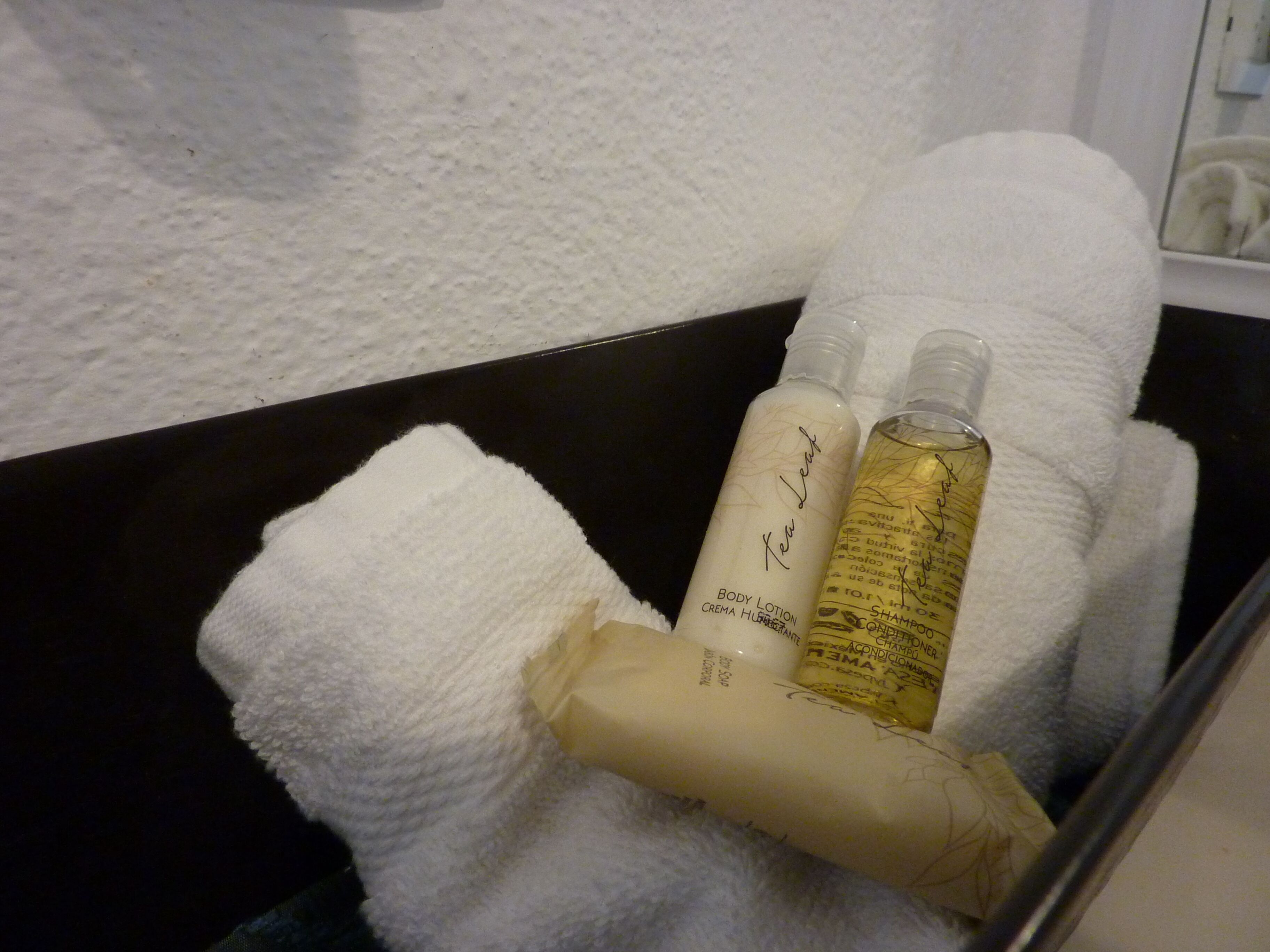 Et badeværelse med et hvidt håndklæde og toiletartikler, herunder bodylotion, shampoo og balsam.