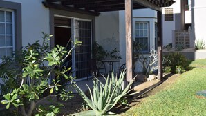 Una casa con un porche cubierto, un pequeño jardín con diversas plantas y una puerta que da al interior.