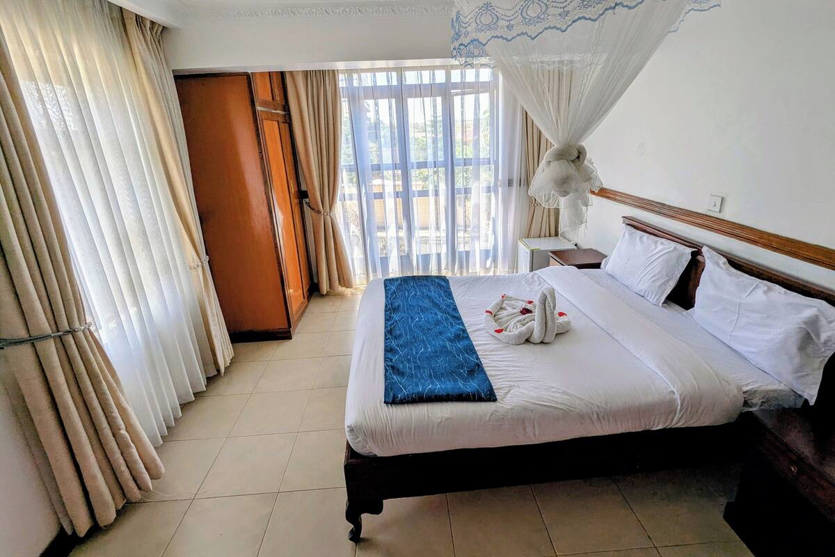 Ein Hotelzimmer mit Bett, Vorhängen, Nachttisch und Fenster mit Blick.