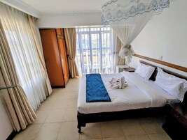 A hotel room with a bed, curtains, a nightstand, and a window with a view.