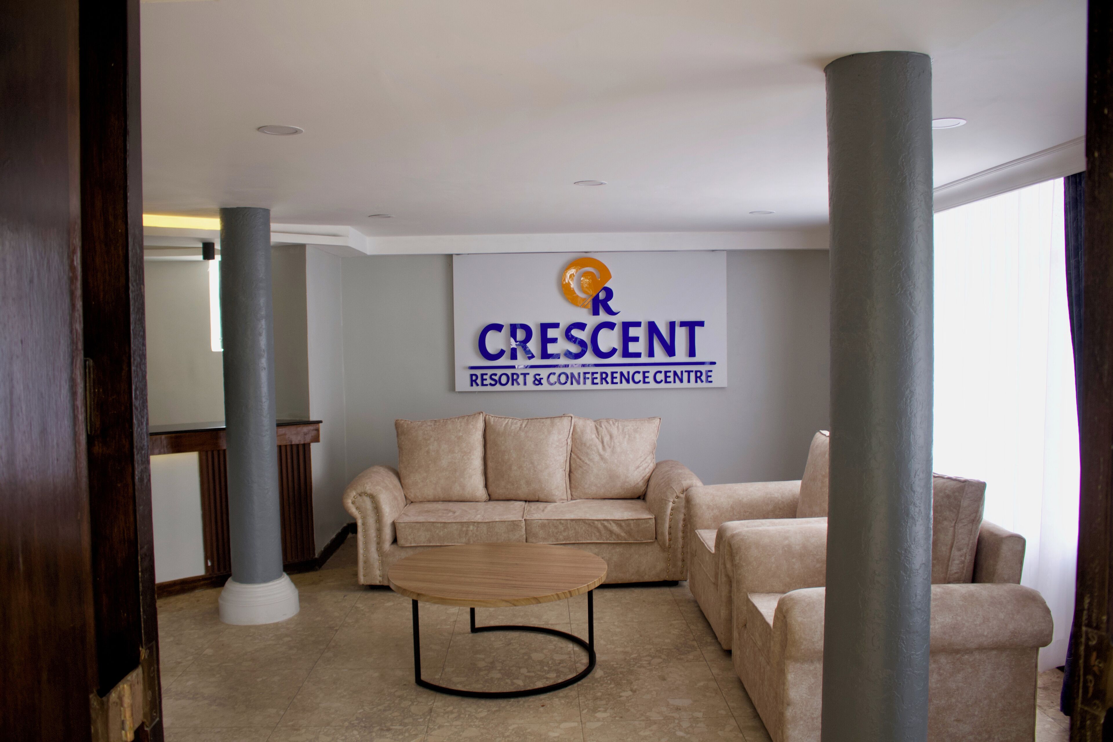 Un salón de conferencias con un sofá color beige, una mesa de centro de madera y un cartel que dice "CRESCENT RESORT & CONFERENCE CENTRE".