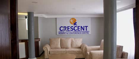 Un salón de conferencias con un sofá color beige, una mesa de centro de madera y un cartel que dice "CRESCENT RESORT & CONFERENCE CENTRE".