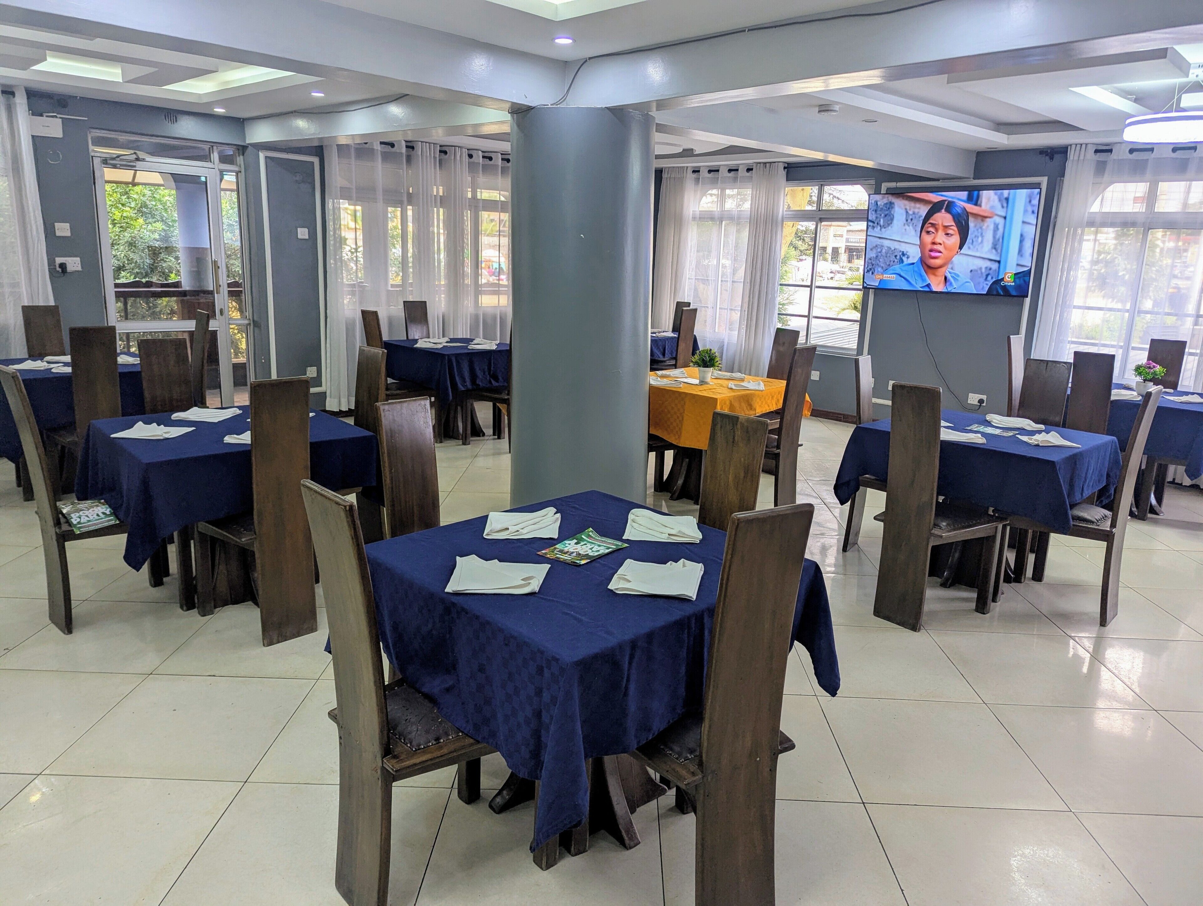 Un espace repas avec des tables dressées pour les invités, un écran de télévision et une vue sur l’extérieur.