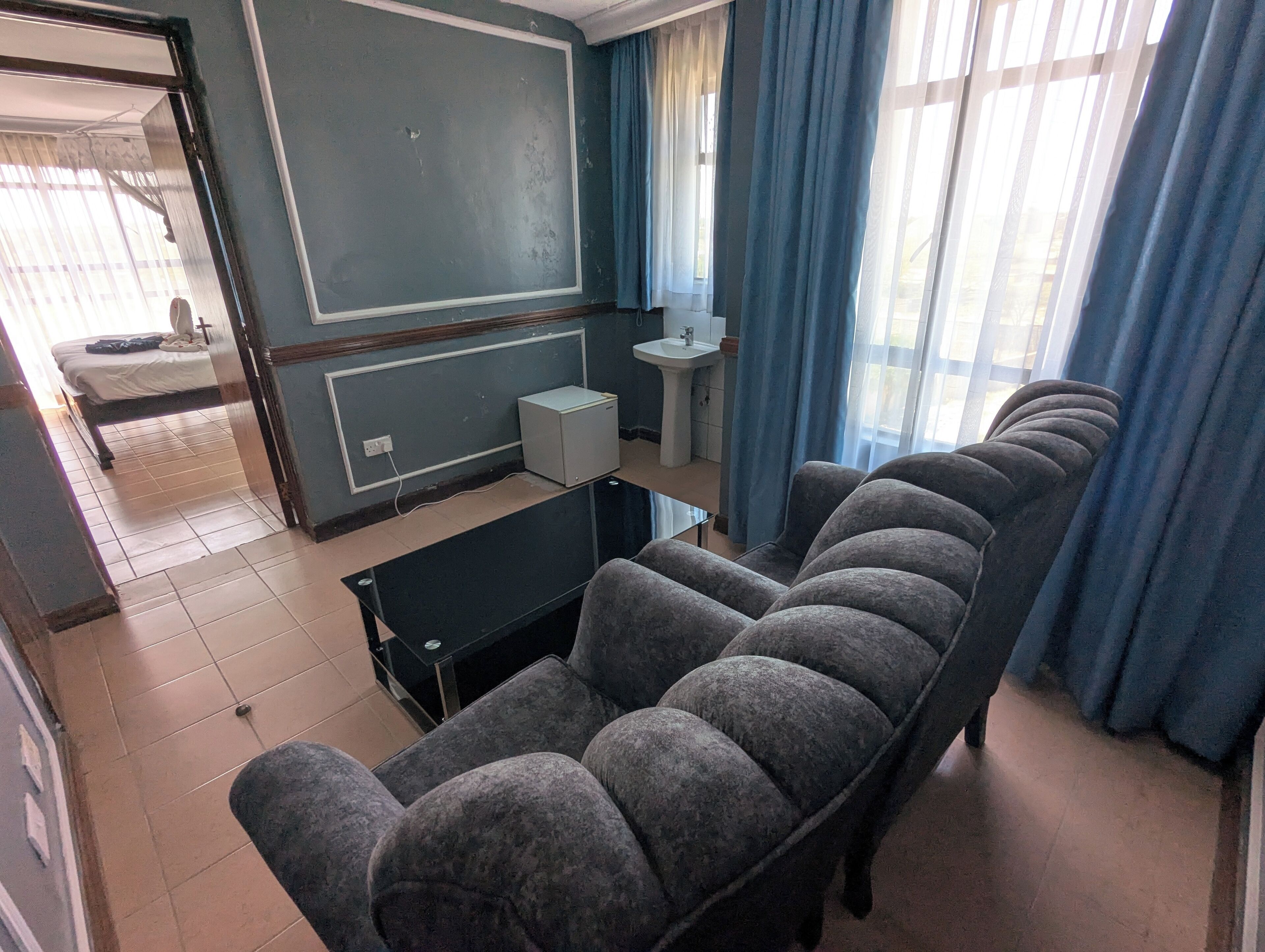 A room with a sofa, a small table, a bed, a sink, and a window with curtains.