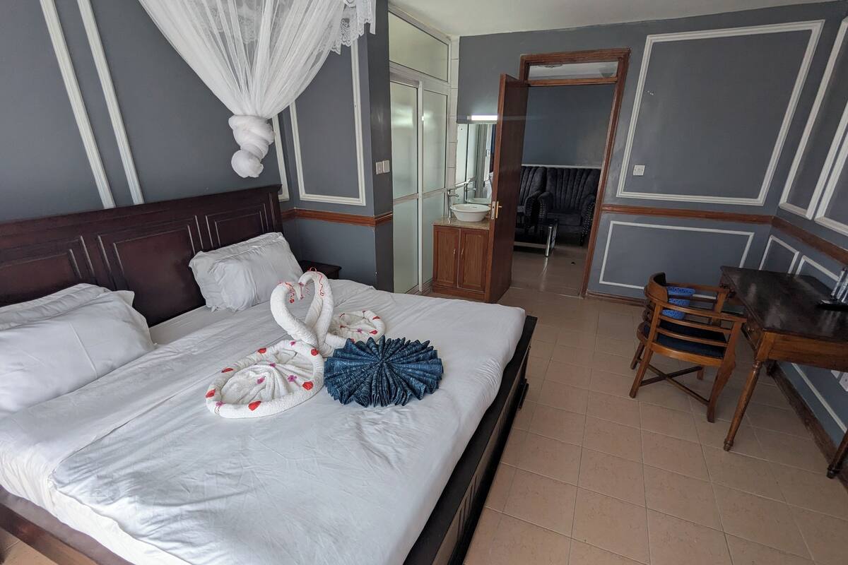 Ein Hotelzimmer mit einem großen Bett, einem hölzernen Nachttisch, einem Sessel und einem durch eine geöffnete Tür einsehbaren Badezimmer.