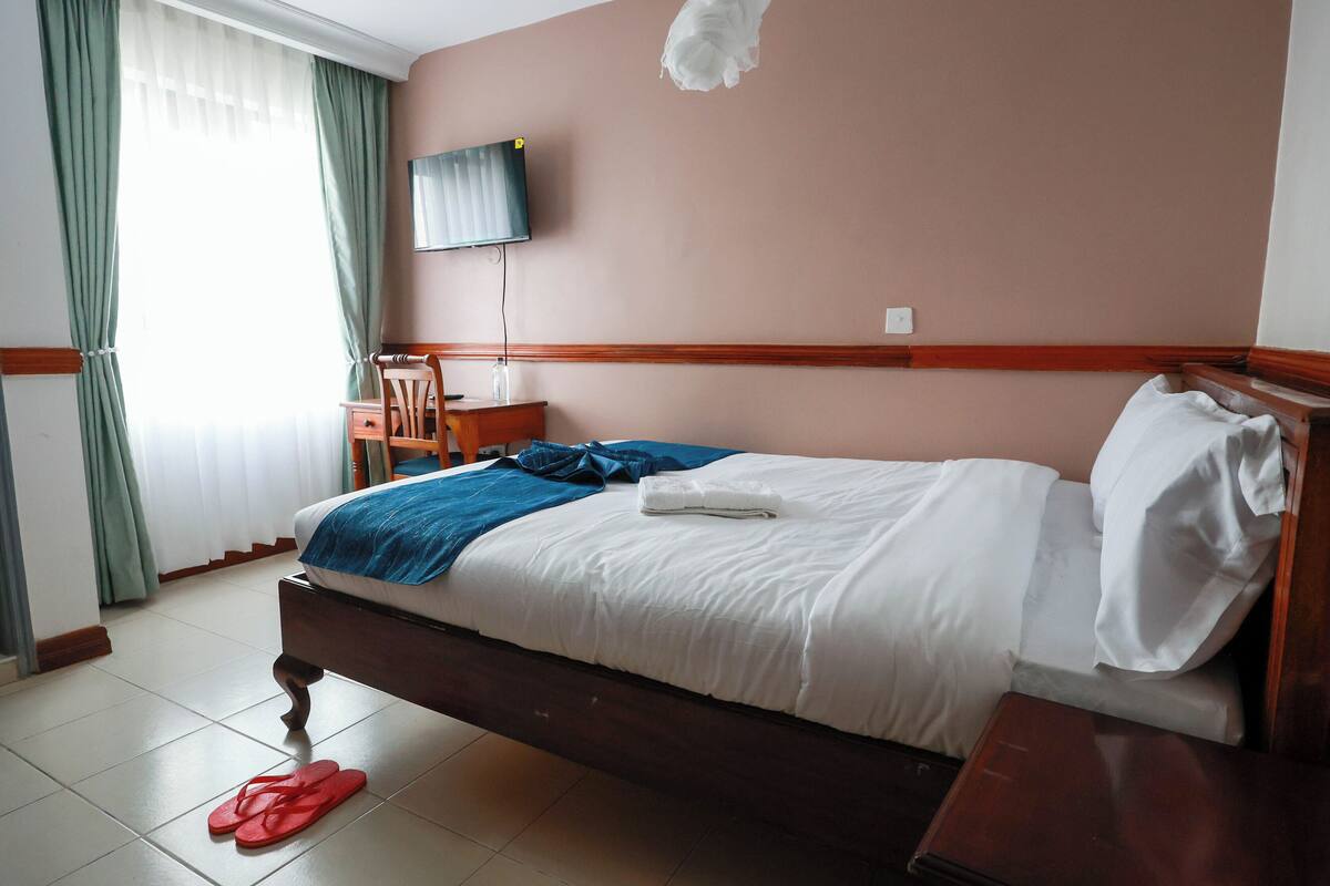 Ein Hotelzimmer mit Bett, Schreibtisch, Stuhl und Fernseher an der Wand.
