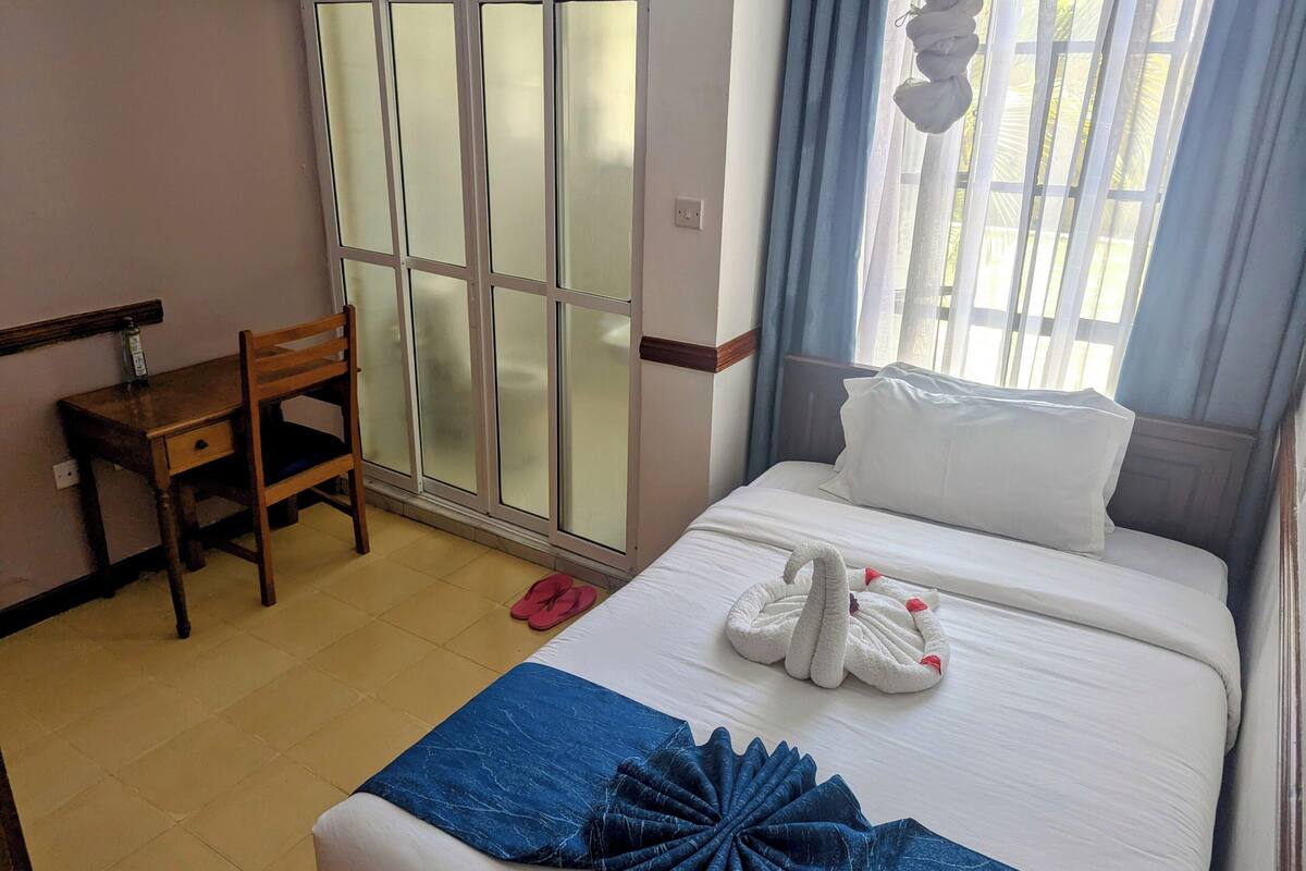 Ein Hotelzimmer mit Bett, Schreibtisch, Stuhl und einem Fenster mit Vorhängen.
