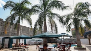 Een buitenterras met ronde tafels en stoelen, parasols en palmbomen.