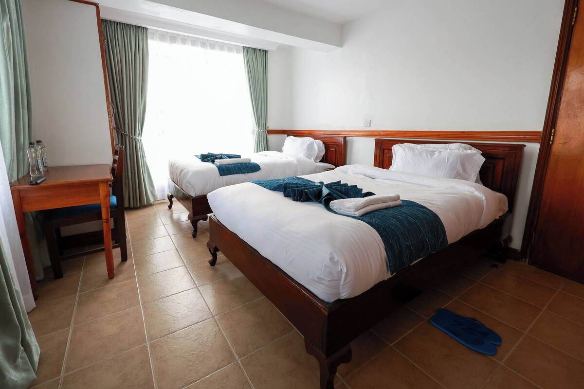 Ein Hotelzimmer mit zwei Betten, einem Holztisch und einem Fenster mit Vorhängen.